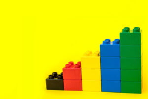 Bar graphs plastic building blocks toy bricks on yellow background.